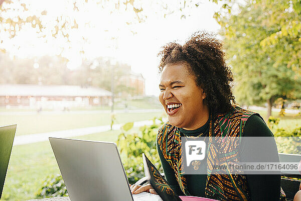 Weibliche Studentin lachend beim Online-Studium durch Laptop in College-Campus