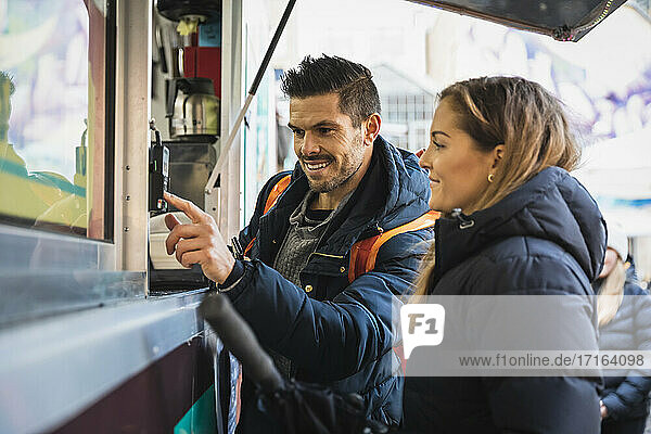 Lächelnder Mann beim kontaktlosen Bezahlen  der neben einer Frau am Foodtruck steht