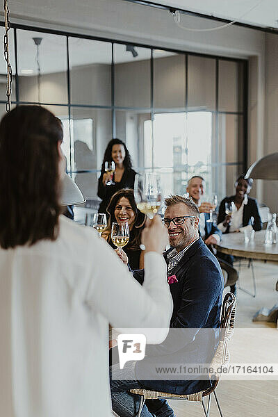 Weibliche Unternehmerin mit Weinglas blickt auf Kollegen während der Firmenfeier