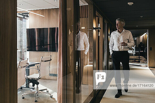 In voller Länge von Senior Geschäftsmann hält Glas beim Gehen durch Vorstand Zimmer im Büro
