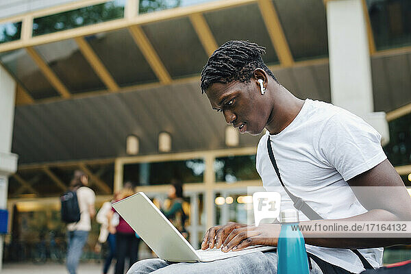 Männlicher College-Student  der auf einem Laptop auf dem Universitätscampus online lernt