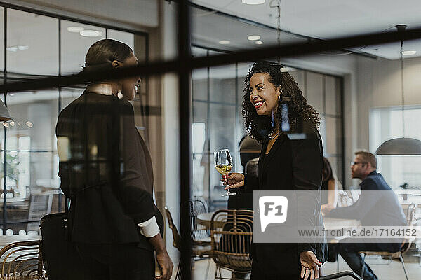 Lächelnde weibliche Kollegen  die sich unterhalten  während sie ein Weinglas im Büro während einer Party halten