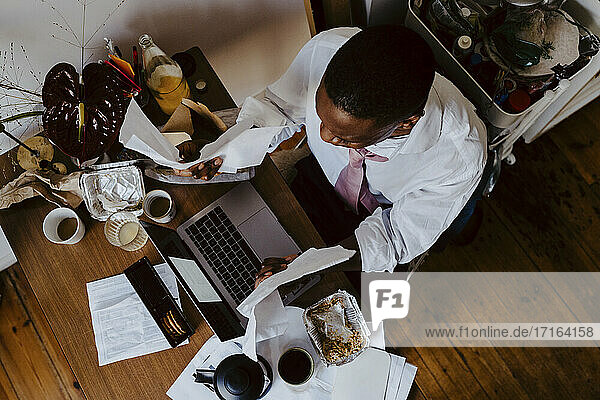 Direkt über der Aufnahme eines männlichen Unternehmers  der einen Laptop am Tisch im Wohnzimmer benutzt