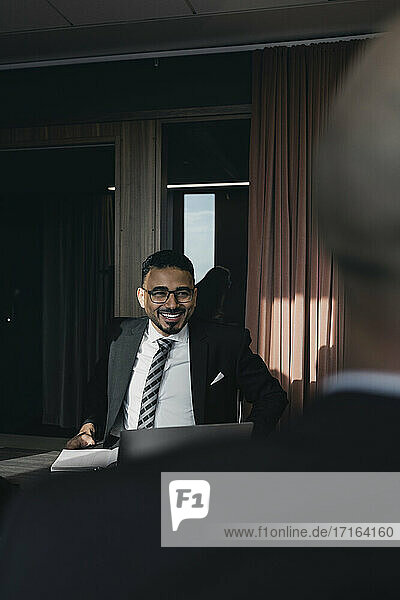 Lächelnder Geschäftsmann  der einen männlichen Kollegen im Vorstandszimmer während einer Besprechung anschaut