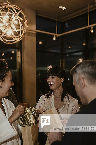 Male and female colleagues laughing while holding gift bags at company during party