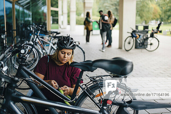 Junge Studentin beim Entriegeln des Fahrrads an der Parkstation auf dem Campus