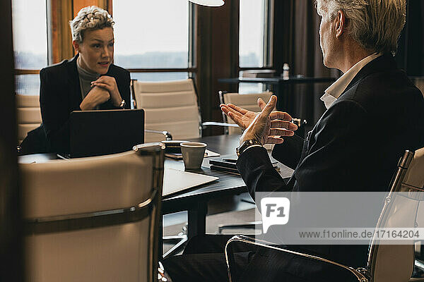 Geschäftsfrau  die der Strategie eines älteren Geschäftsmannes zuhört  während sie am Konferenztisch im Sitzungssaal sitzt