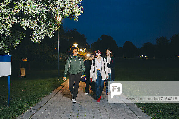 Glückliche männliche und weibliche Freunde zu Fuß in Campus in der Nacht