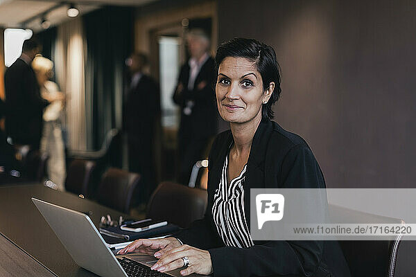 Portrait of smiling businesswoman sitting with laptop at conference table in board room