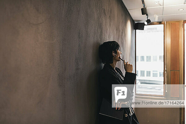 Nachdenkliche Geschäftsfrau schaut weg  während sie sich im Büro an die Wand lehnt