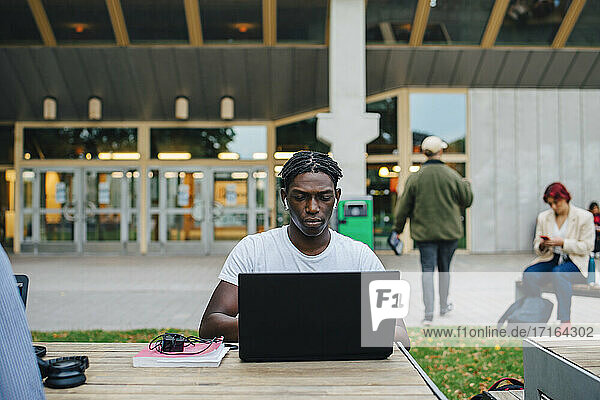 Junger männlicher Student konzentriert sich beim E-Learning am Laptop in der Universität