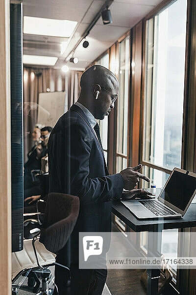 Seitenansicht des glatzköpfigen männlichen Unternehmers mit Laptop im Sitzungssaal durch eine Glaswand gesehen