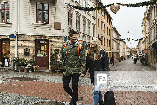 Lächelndes Paar hält Hände beim Gehen auf der Straße in der Stadt