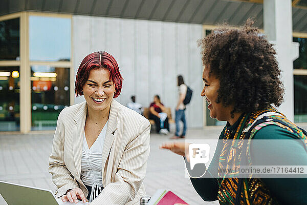 Weibliche Studenten lachen beim gemeinsamen Lernen auf dem Universitätscampus