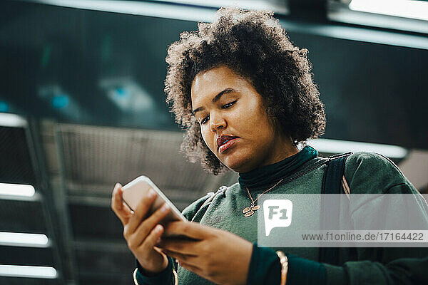 Weibliche Studentin  die in der U-Bahn eine Textnachricht auf einem Smartphone schreibt