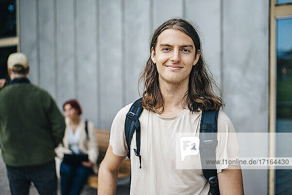 Porträt eines lächelnden männlichen Studenten vor einer grauen Wand auf dem Campus