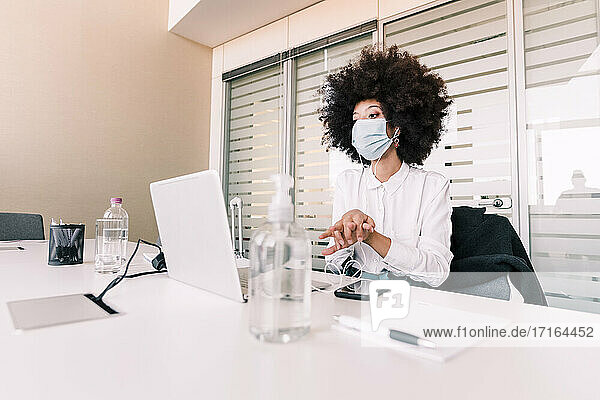 Geschäftsfrau trägt Gesichtsmaske und benutzt Handdesinfektionsmittel