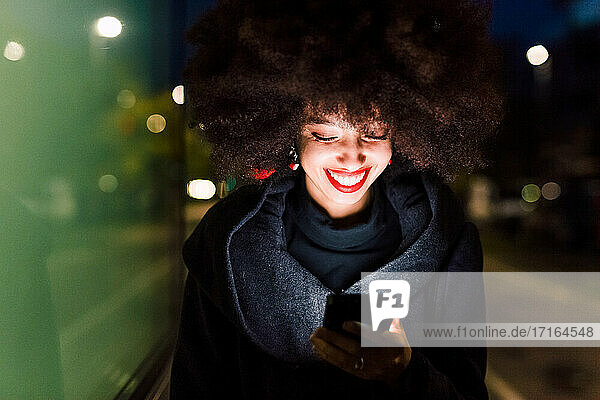 Young woman looking at phone and smiling  illuminated at night
