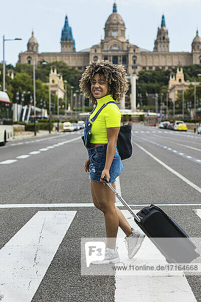 Smiling female wheeling luggage while walking on street at city
