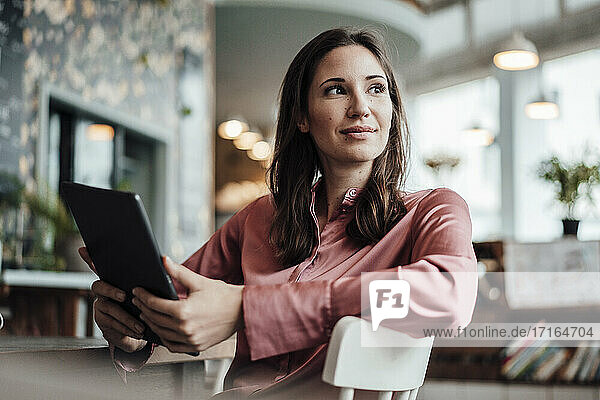 Weibliche Fachkraft mit digitalem Tablet  die wegschaut  während sie in einem Café sitzt