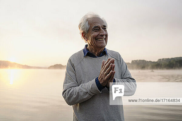 Lächelnder Mann  der mit verschränkten Händen am See steht