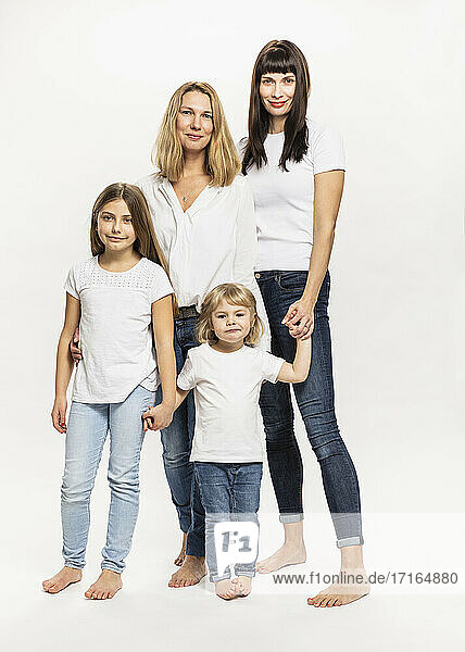 Smiling women standing with daughters against white background in studio
