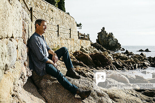 Nachdenklicher Mann auf einem Felsen am Strand sitzend an einem sonnigen Tag