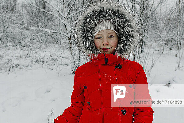 Smiling girl in warm clothing standing at forest during vacations