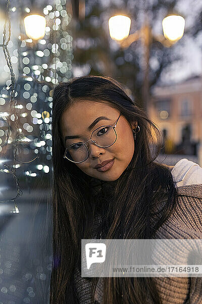 Young woman leaning on illuminated glass wall at dusk