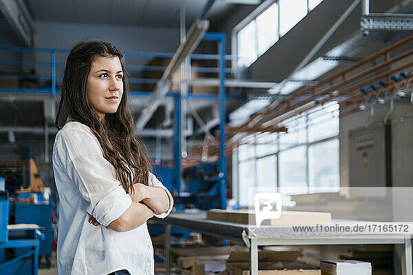 Confident female expertise with arms crossed looking away while standing at industry