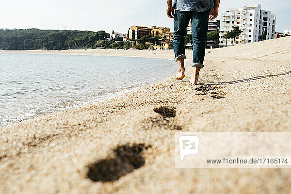 Älterer Mann  der an einem sonnigen Tag auf dem Sand am Strand spazieren geht