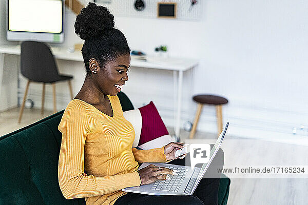Smiling young woman using laptop for online shopping in living room at home