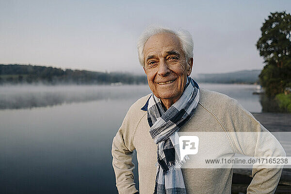 Smiling man wearing scarf staring while standing against lake