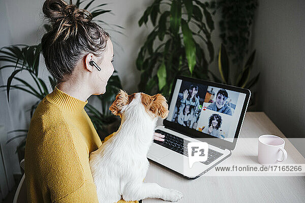 Woman talking with friends on video conference over digital tablet while sitting with pet at home