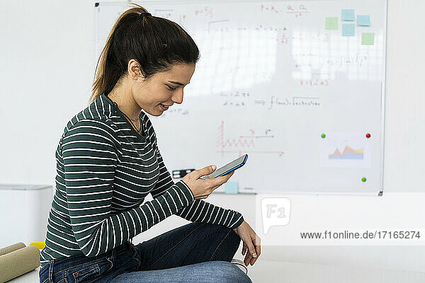 Lächelnde junge Geschäftsfrau  die ein Smartphone am Arbeitsplatz benutzt