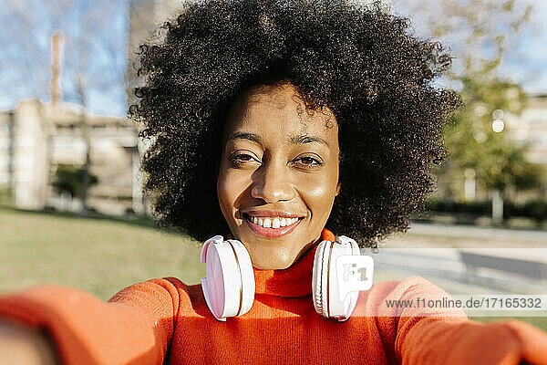 Lächelnde Afro-Frau mit Kopfhörern macht ein Selfie im Park an einem sonnigen Tag