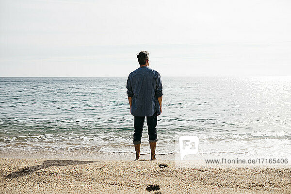 Mann steht an einem sonnigen Tag am Strand am Meer