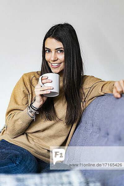 Woman drinking coffee while sitting on sofa at home