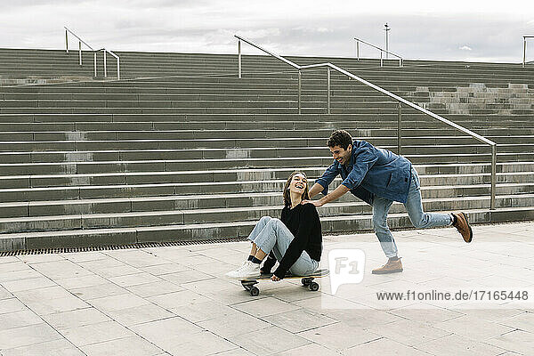 Man pushing woman sitting on skateboard