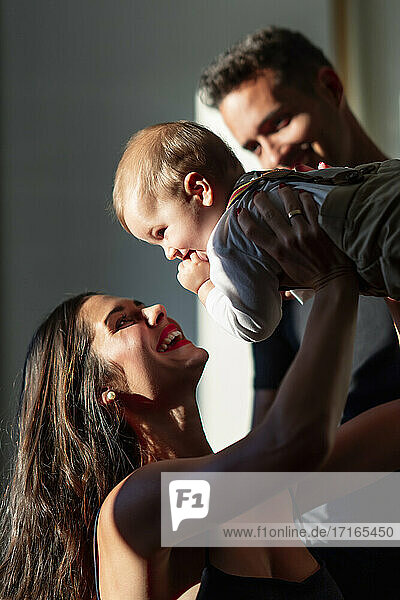 Smiling woman playing with baby boy while standing by man at home