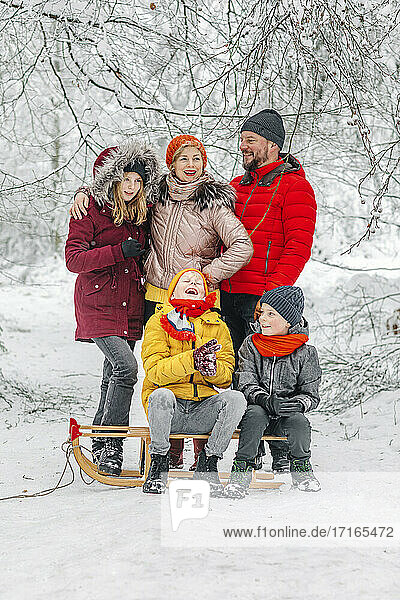 Parents standing by children sitting on sleigh in forest during winter