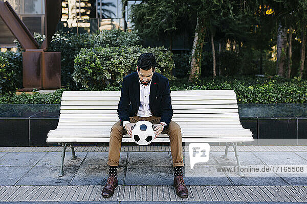 Mid adult businessman holding soccer ball while sitting on bench