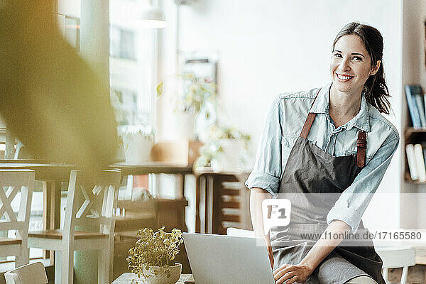 Happy female owner by laptop at table in cafe
