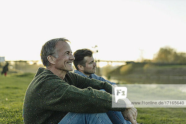 Smiling father spending leisure time with son on grass at riverbank