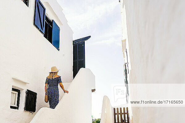 Ältere Frau klettert auf die Stufen eines weiß getünchten Gebäudes im Dorf Binibeca  Menorca  Spanien
