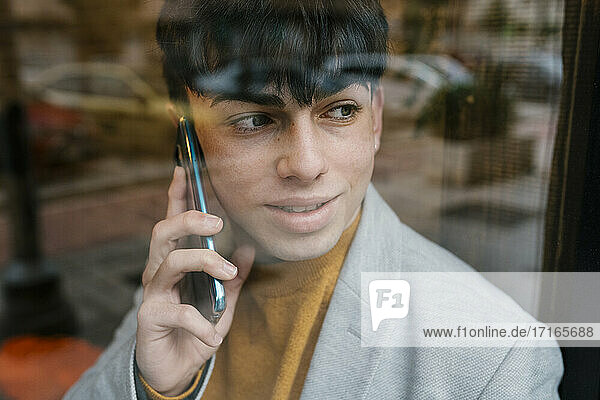 Mann spricht mit seinem Smartphone und schaut durch das Fenster eines Cafés