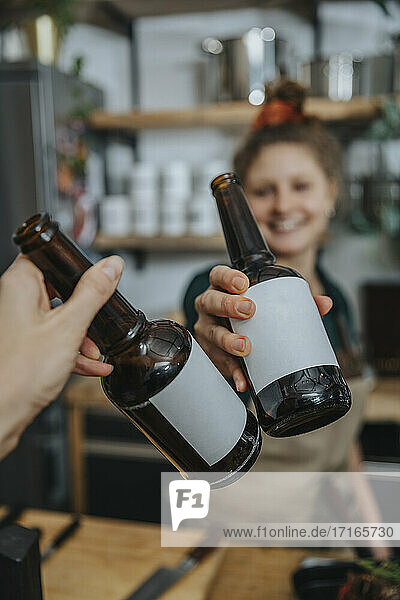Chef toasting beer bottle with woman while standing in kitchen