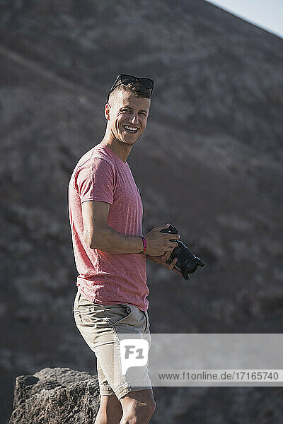 Happy male tourist holding camera at Femes Viewpoint on sunny day  Lanzarote  Spain