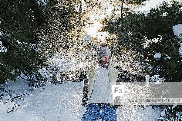 Cheerful man with arms outstretched playing on snow during winter