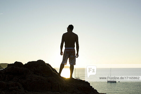 Man looking at view while stancing on rock during sunset at Minorca beach in Spain